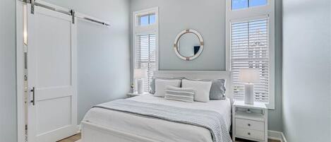 A bedroom with a bed, bedside tables, a mirror, and a window with blinds.