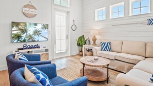 Ein Wohnzimmer mit einem beigen Sofa, einem blauen Sessel, einem Couchtisch und einem an der Wand befestigten Fernseher.