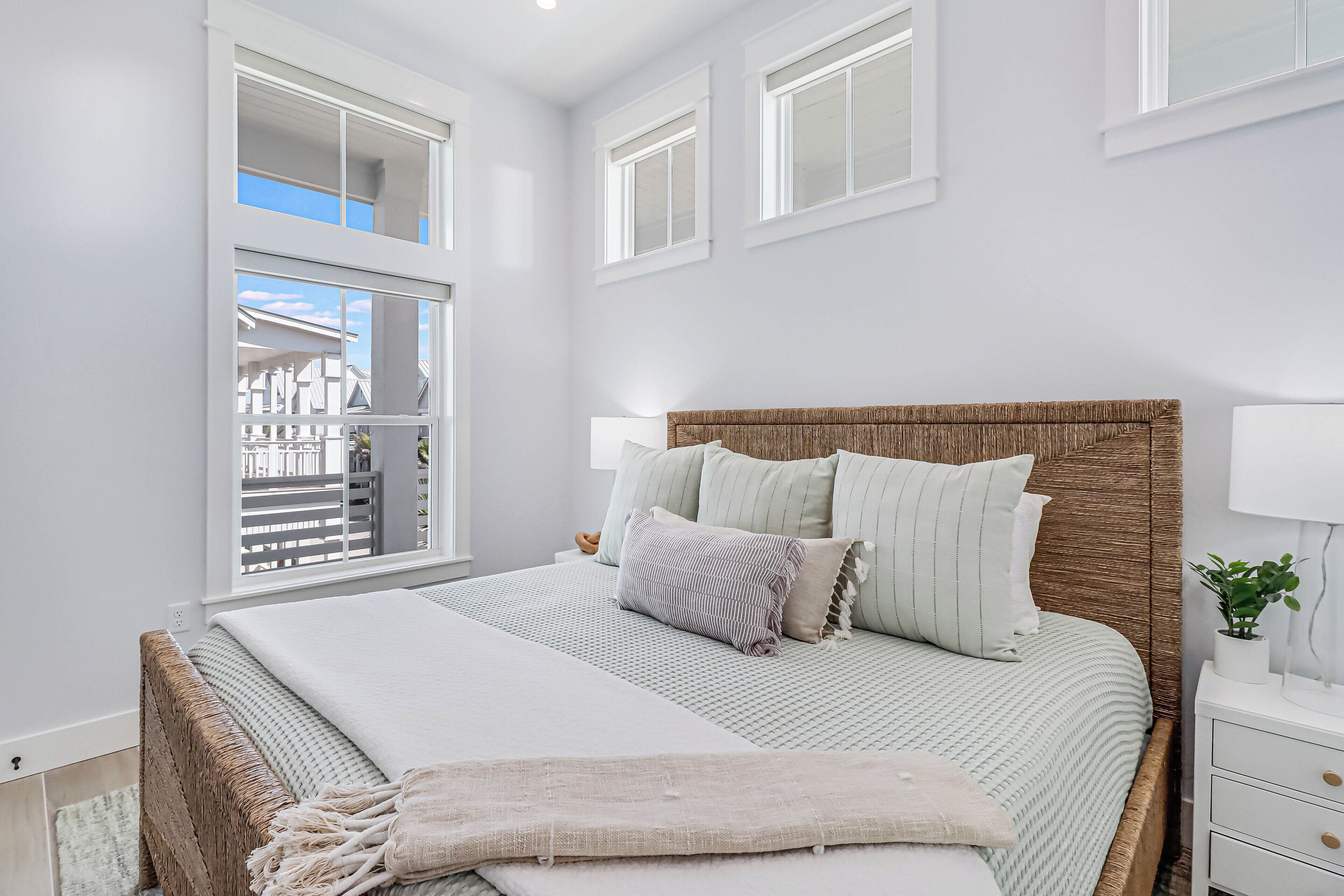 A bedroom with a large bed, a bedside table, a window with a view, and a nightstand with a lamp.
