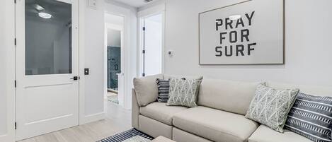 Una sala de estar moderna con un sofá color beige, almohadones estampados, una mesita de centro y un letrero enmarcado en la pared.