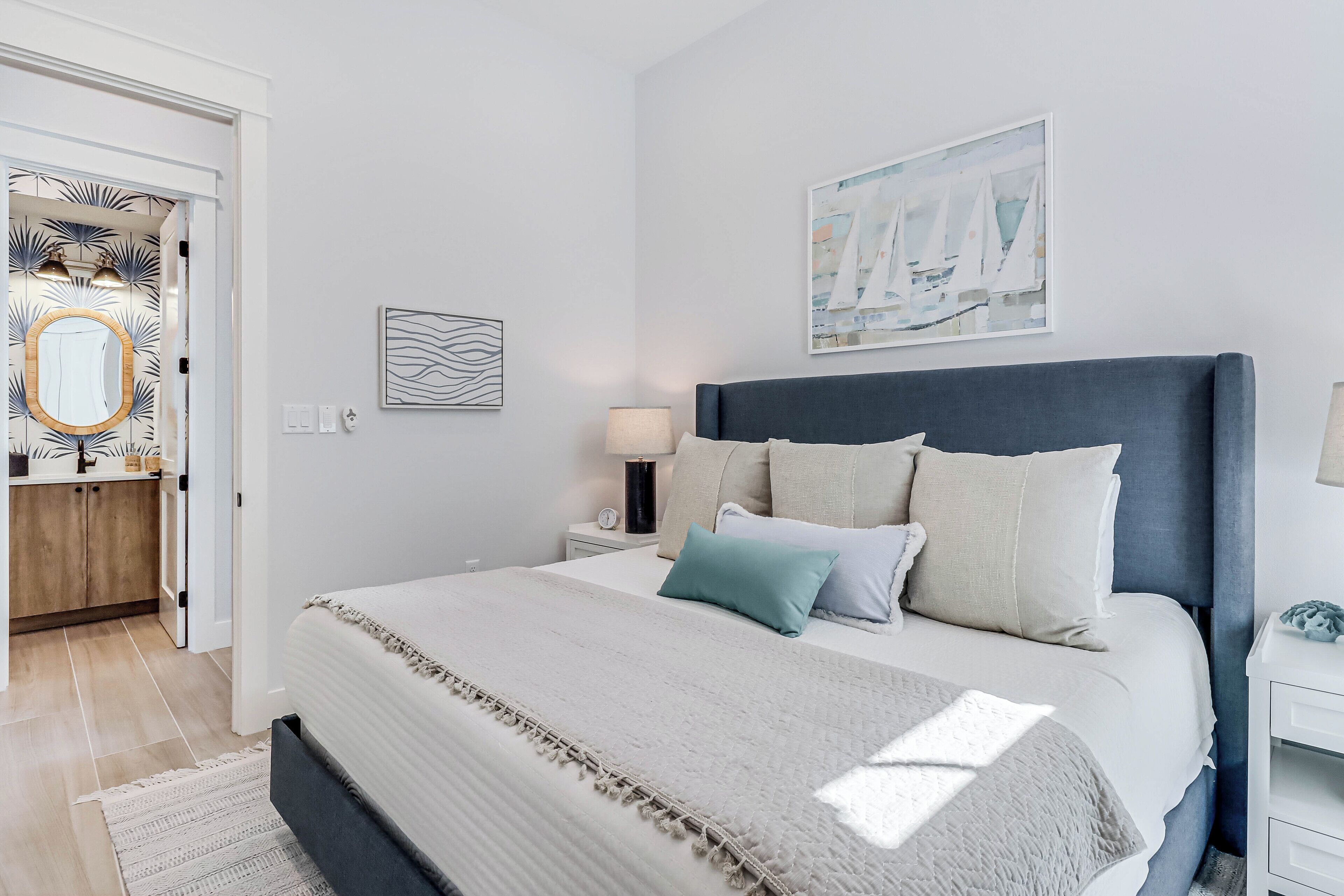 A bedroom with a large bed, a bedside table, a nightstand, a mirror, and a door leading to a bathroom.