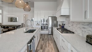 A modern kitchen with white cabinetry, stainless steel appliances, and a large island with a sink. - The Great White 306 DAR (Port Aransas)