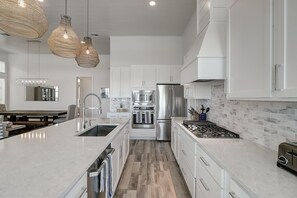 Een moderne keuken met witte kasten, roestvrijstalen apparatuur en een groot schiereiland met een spoelbak.