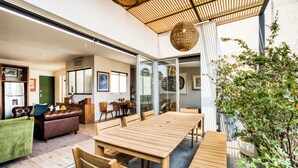 Ein modernes Wohnzimmer mit einem großen Holztisch und Stühlen, einem grünen Sofa und einem Essbereich mit einer Glastür, die auf einen Balkon führt.