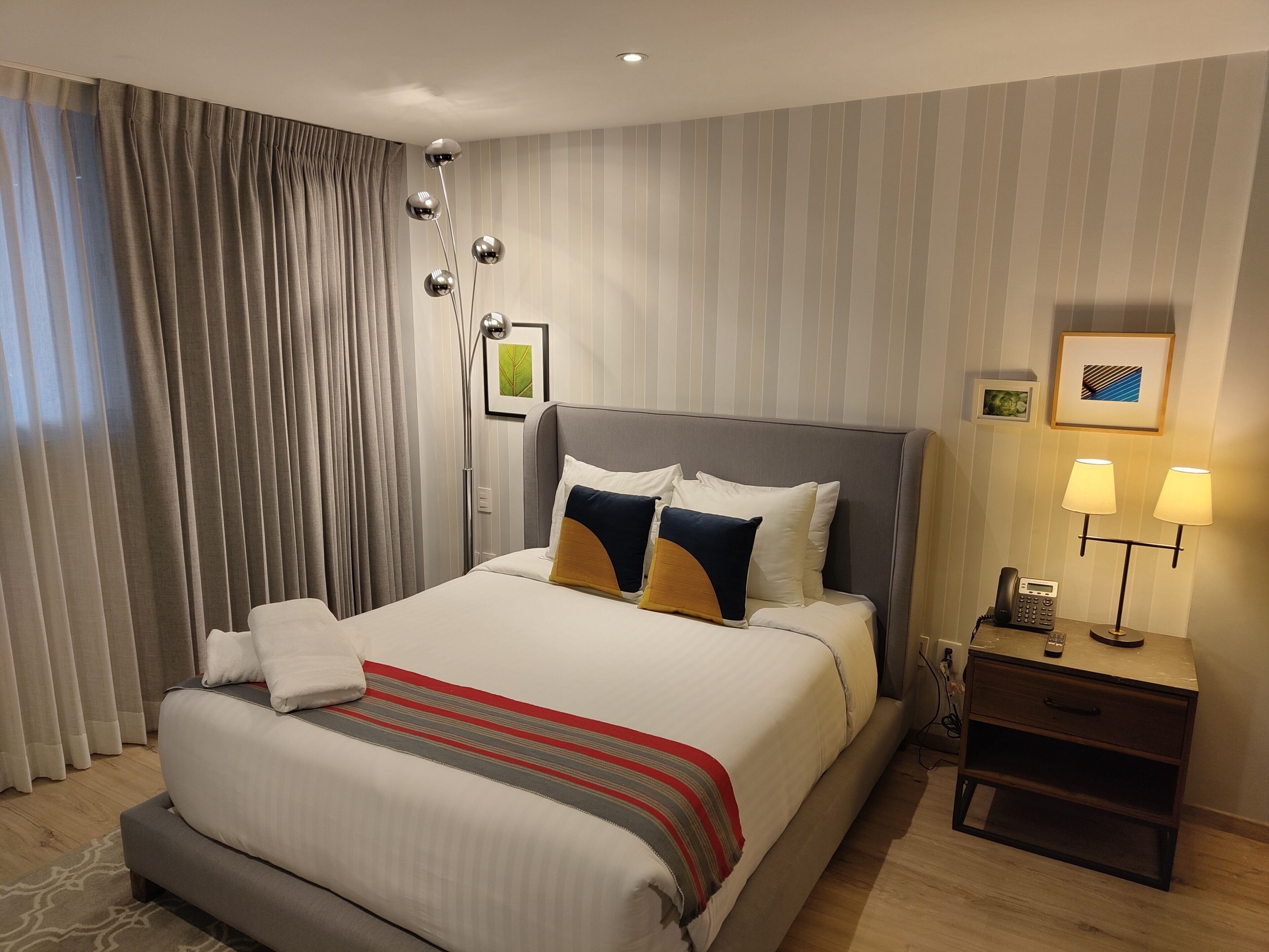 A hotel room with a large bed, a bedside table with a lamp, and a wall-mounted phone.
