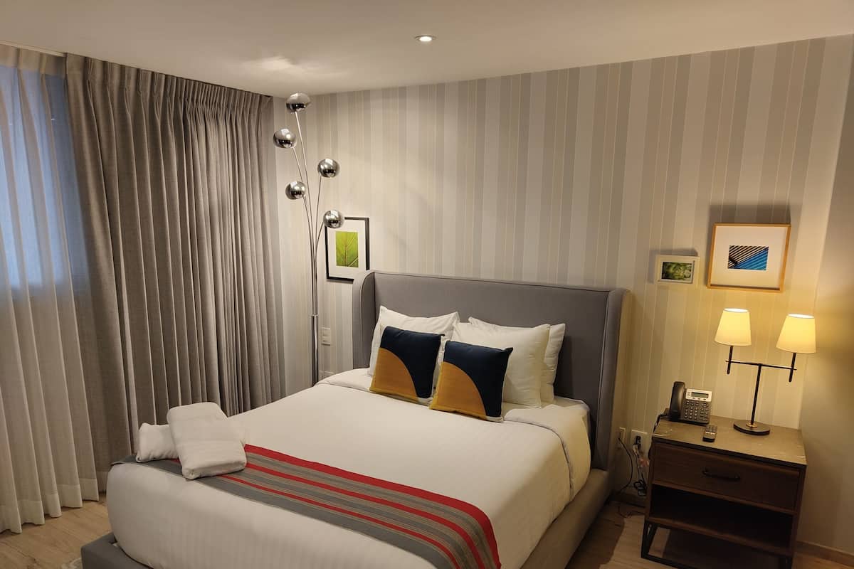 A hotel room with a large bed, a bedside table with a lamp, and a wall-mounted phone.