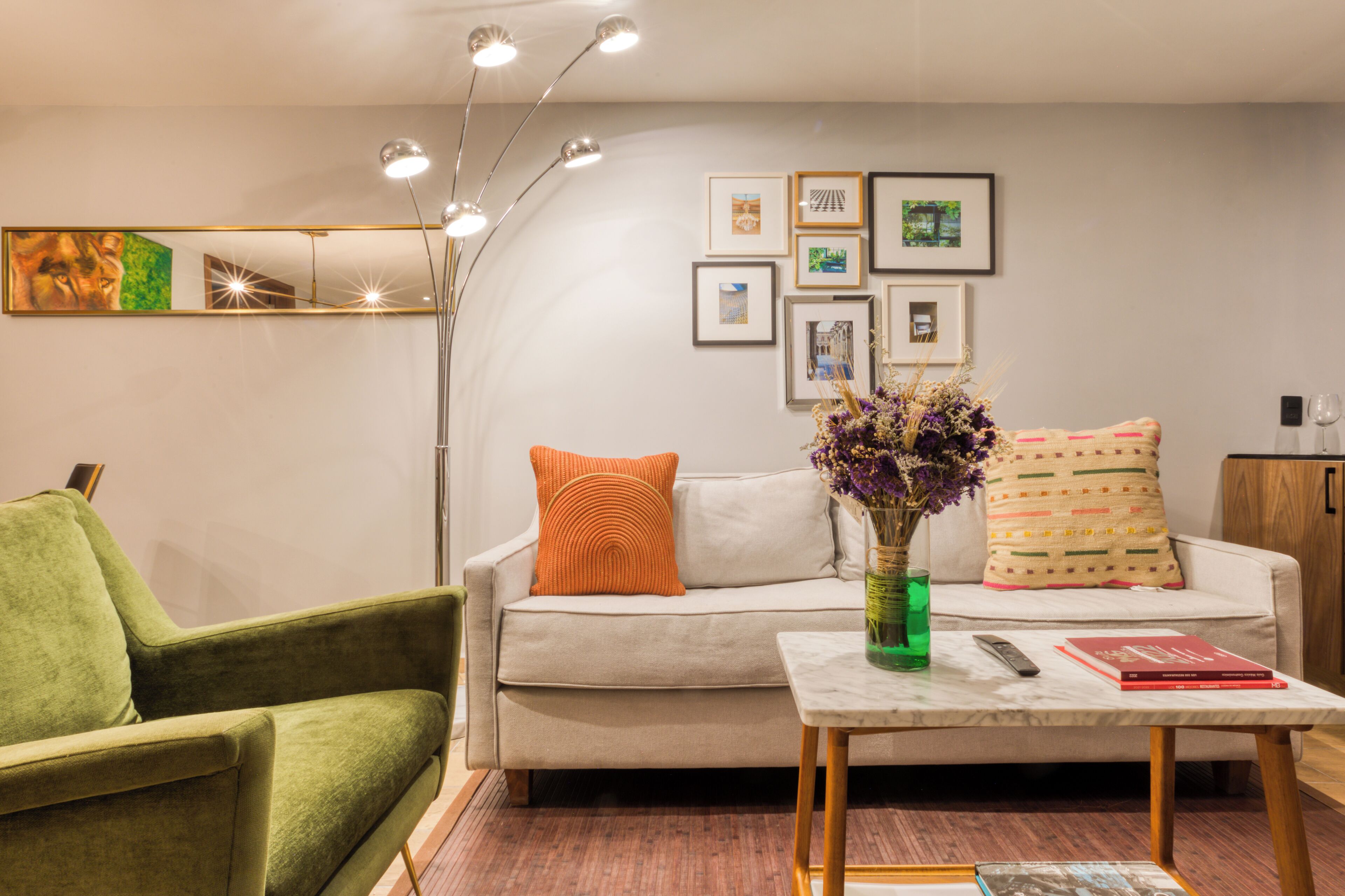 Un salon moderne avec un canapé, un fauteuil vert et une table basse agrémentée d’un vase et d’une télécommande.