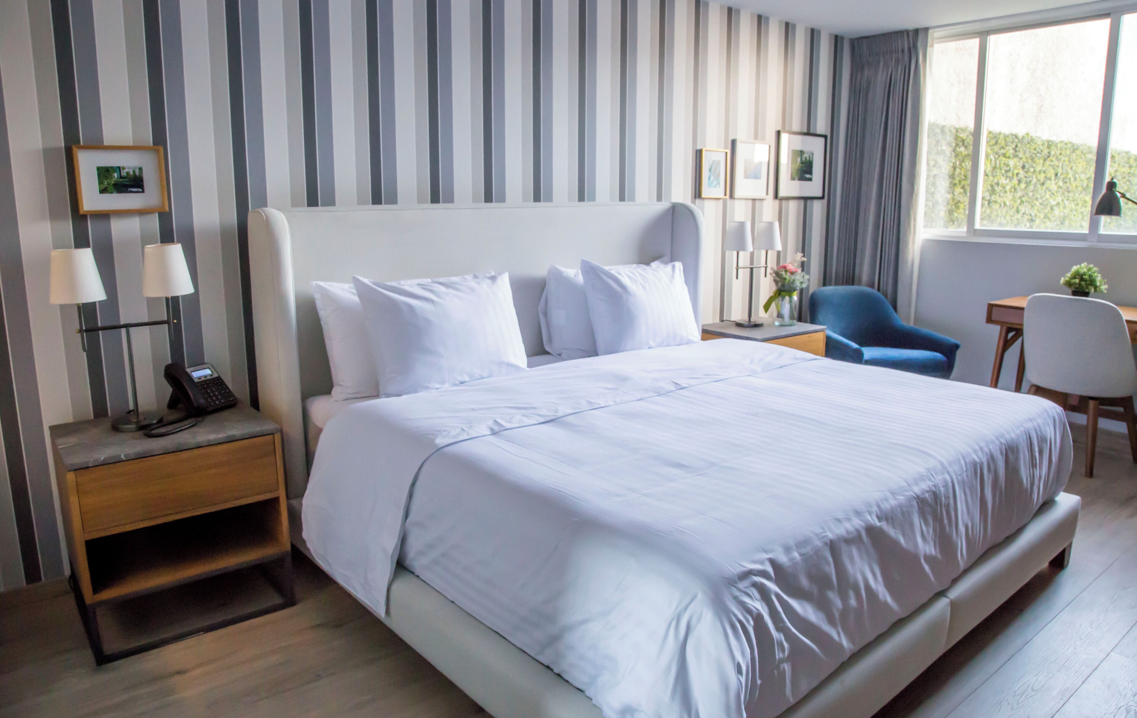 A hotel room with a large bed, a bedside table with a phone, a lamp, and a chair.