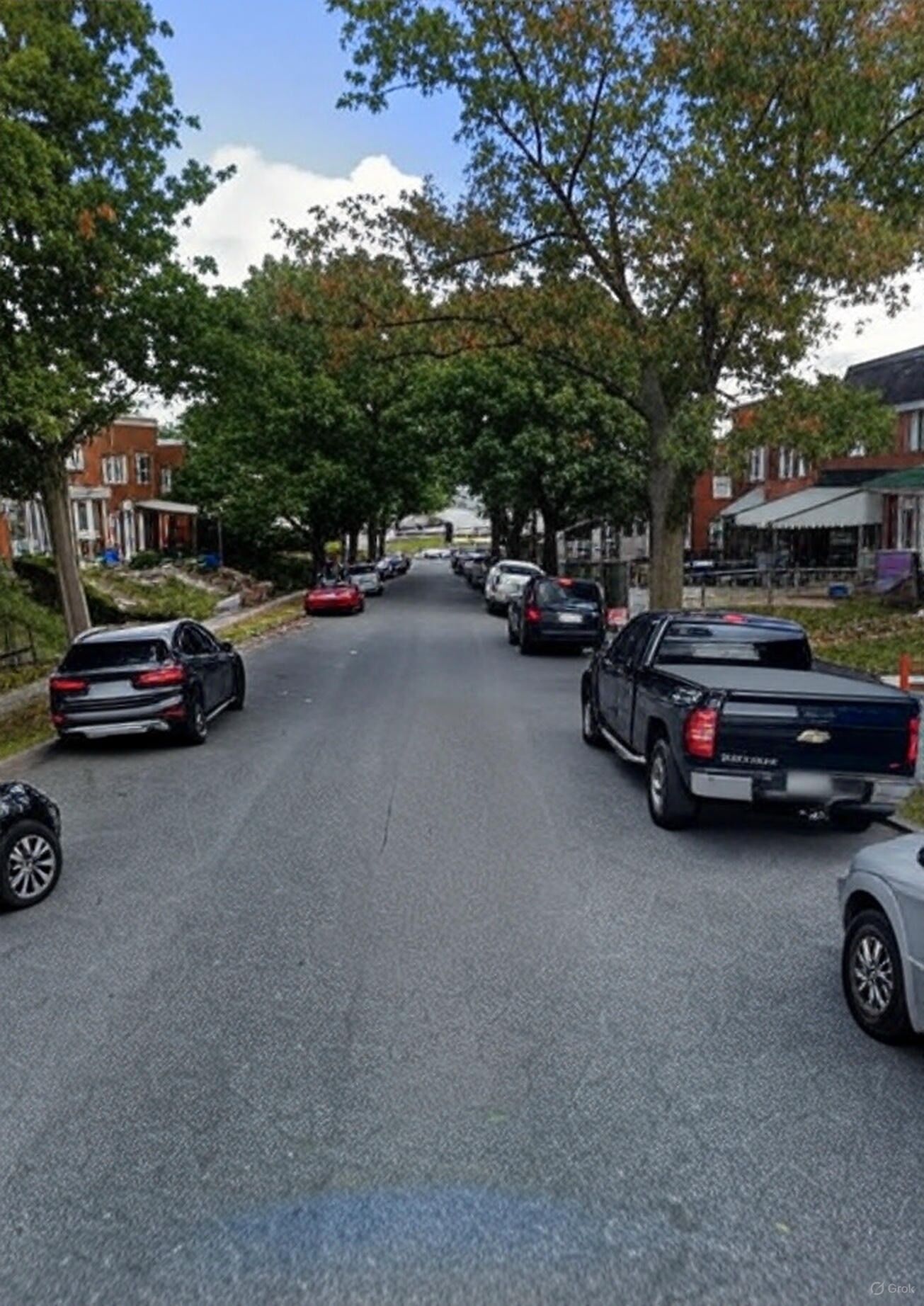 Een straat met geparkeerde auto's en bomen, met gebouwen aan beide zijden.