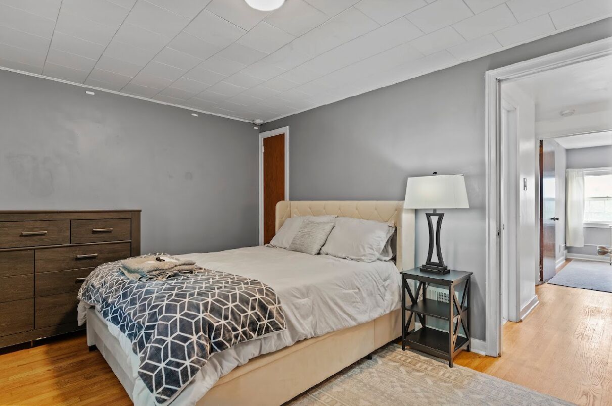 Un dormitorio con cama, mesita de noche, cómoda y puerta que da a otra habitación.