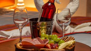 A dining table with a bottle of wine, two glasses, and a fruit and cheese platter.