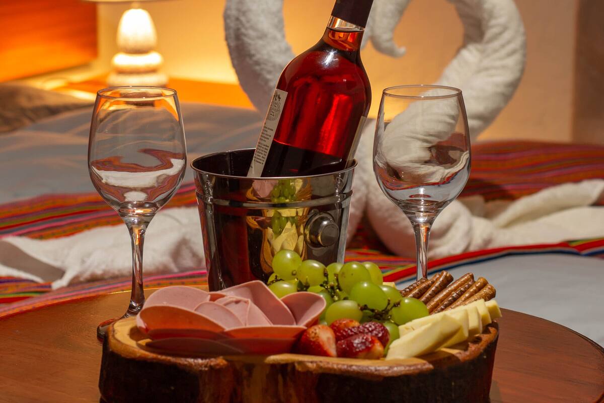 Una mesa de comedor con una botella de vino, dos copas y un plato de fruta y queso.
