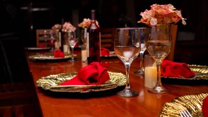 A dining table set with gold-rimmed plates, red napkins, and clear wine glasses.