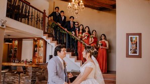 A wedding ceremony in a spacious hall with a staircase, wooden furniture, and a chandelier.