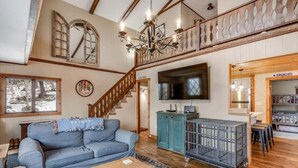 Un salon spacieux avec un canapé bleu, un plancher en bois, une télévision et un escalier menant à l’étage supérieur.
