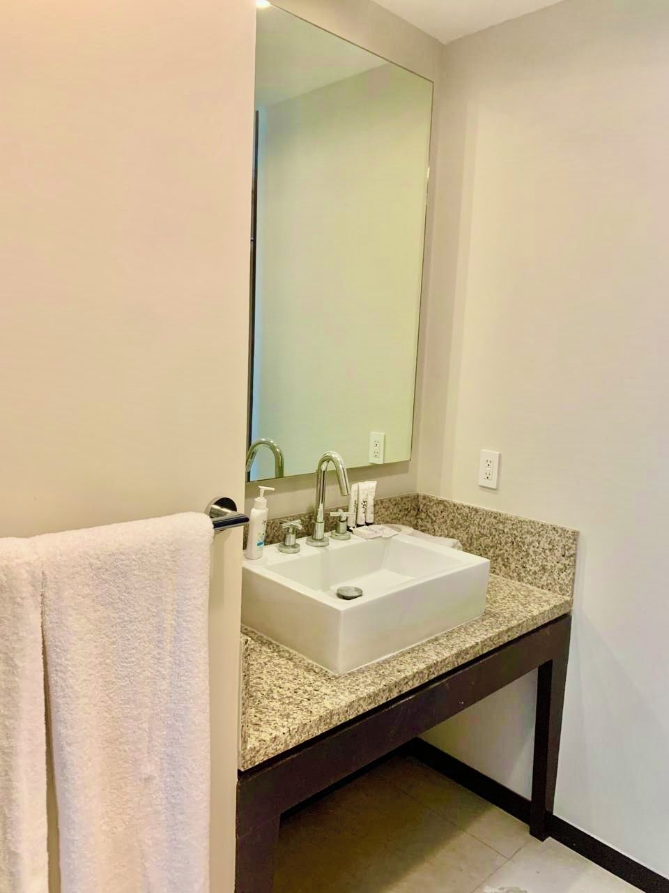 A bathroom with a white sink, a large mirror, and a towel on the left.