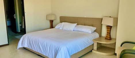A bedroom with a bed, two bedside tables with lamps, a chair, and a door leading to another room.