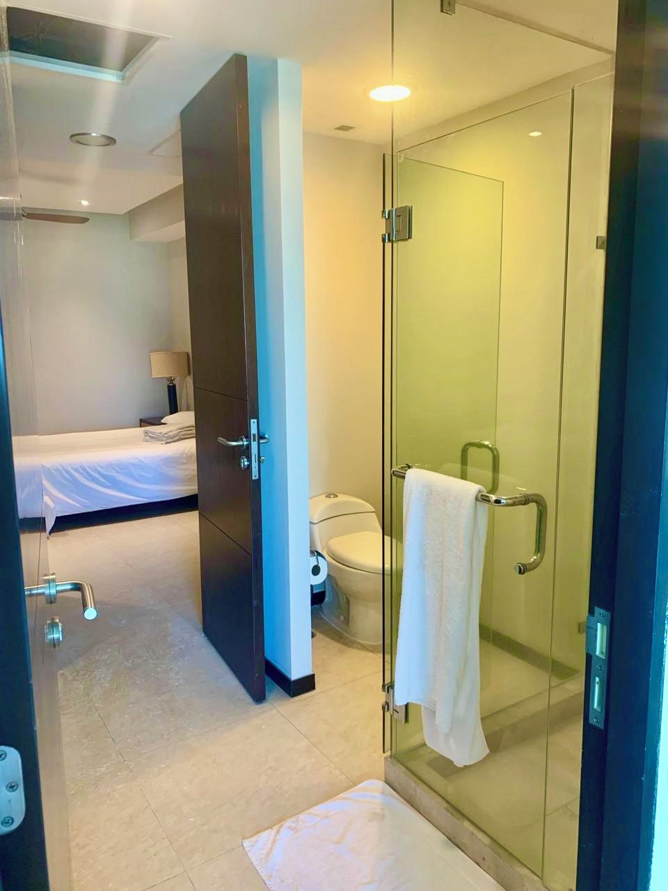 A hotel room with a glass shower enclosure, a bed, a bedside table, and a toilet.