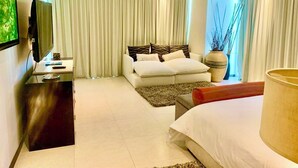 Una habitación de hotel moderna con sofá cama, escritorio con televisor de pantalla plana, mesita de noche y ventana grande con cortinas.