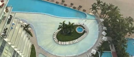 A resort with a pool, lounge chairs, and palm trees.