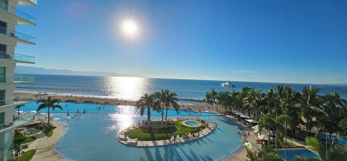 A resort with a large central pool, a smaller pool, and a beach area.