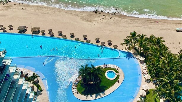 Un resort con una piscina grande, una playa y palmeras.