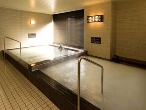 Ein Whirlpoolbereich mit gefliestem Boden, Metallgeländern und Wandleuchten.
