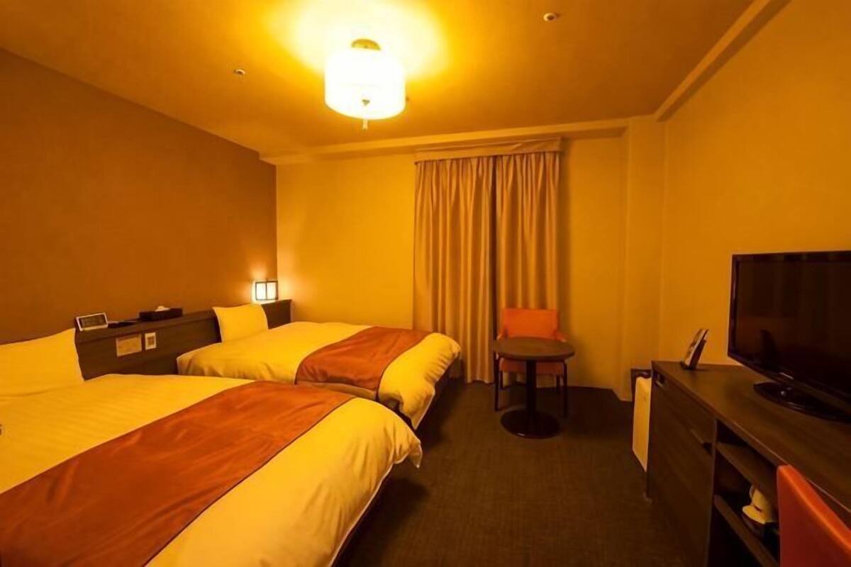 A hotel room with two beds, a television, a desk, and a chair.