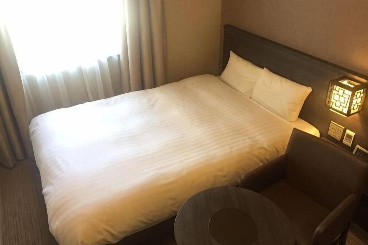 A hotel room with a bed, a round table, and a wall-mounted light fixture.
