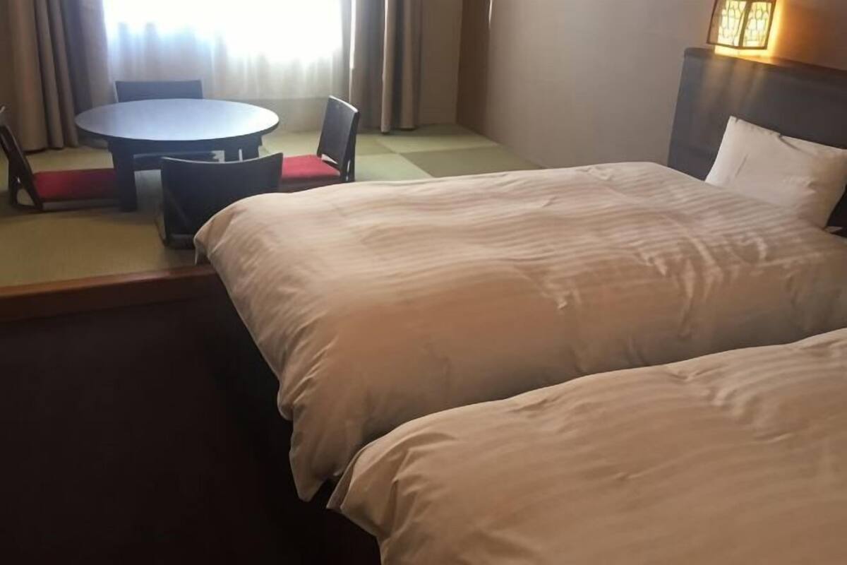 A hotel room with two beds, a round table with chairs, and a view of the outdoors.