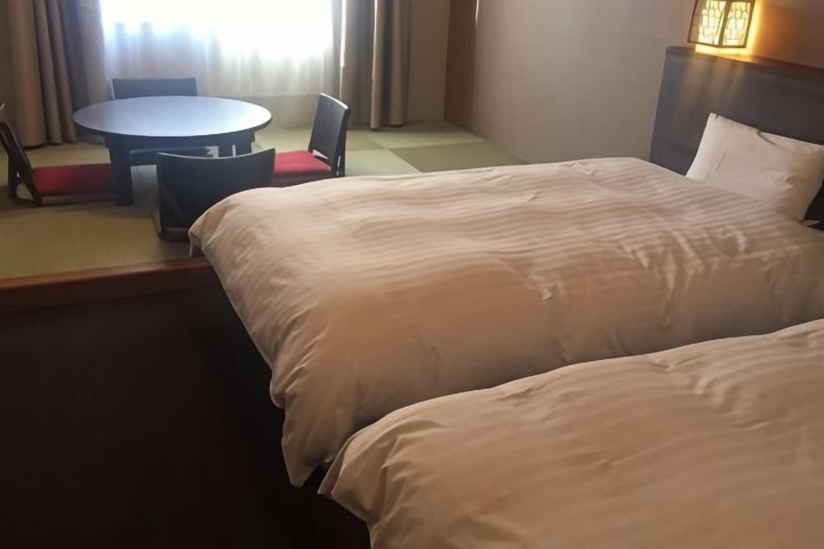 Ein Hotelzimmer mit zwei Betten, einem runden Tisch mit Stühlen und Blick ins Freie.