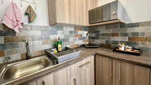 Una cocina con armarios de madera, un lavamanos de acero inoxidable, un microondas y un salpicadero de azulejos.
