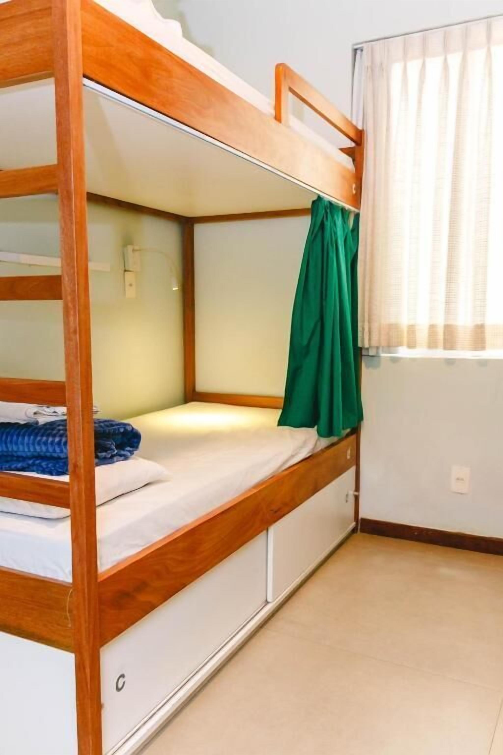 A bunk bed with a wooden frame, a green curtain, and a window with sheer curtains.