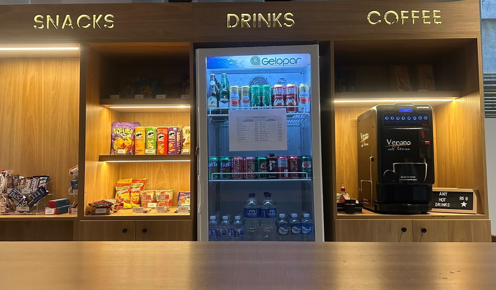 Un distributeur automatique marqué « Gelopar » proposant des collations et des boissons, ainsi qu’une machine à café marquée « Verano café premium », dans un hôtel.