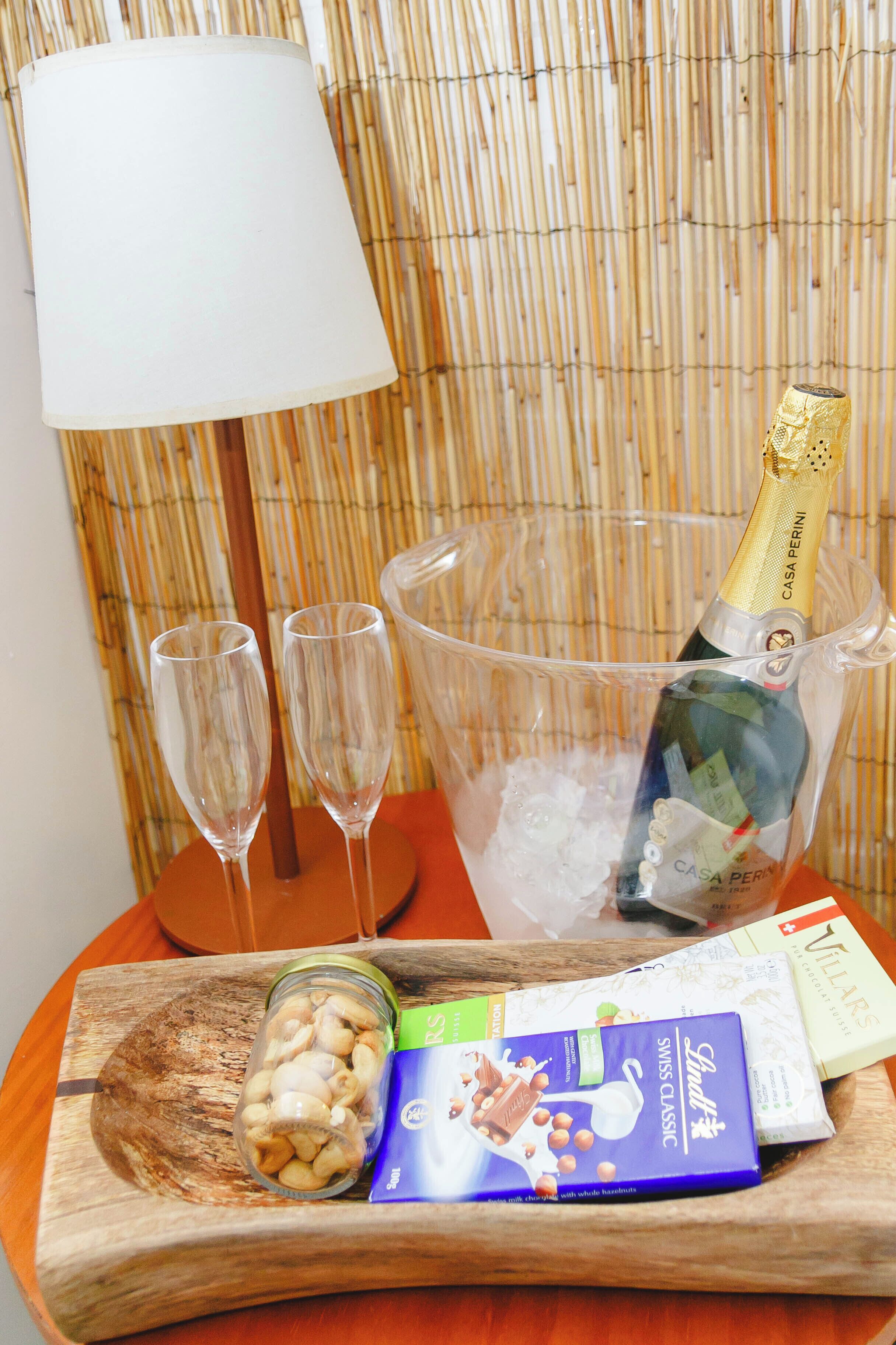 Una mesa con una botella de champán, dos copas, un bol de nueces y una caja de bombones Lindt.