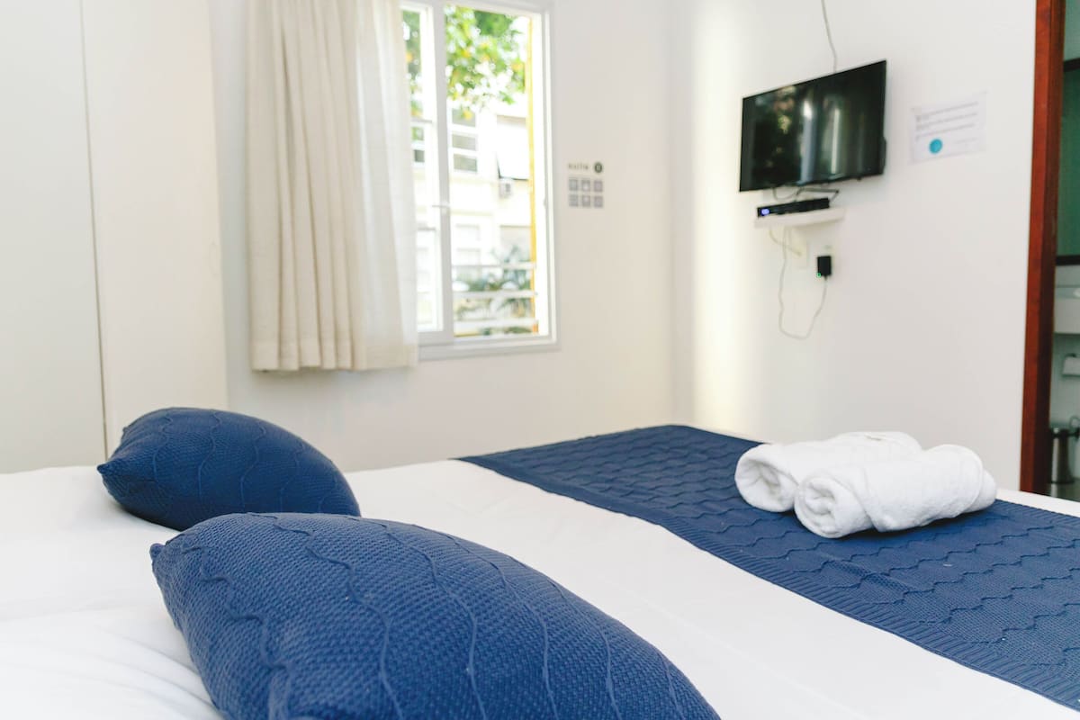 A hotel room with a bed, a television mounted on the wall, and a window with curtains.