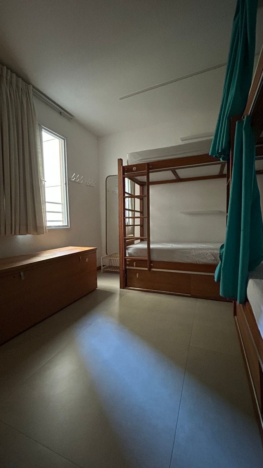 Habitació amb lliteres, una finestra, una panxa i una cortina.