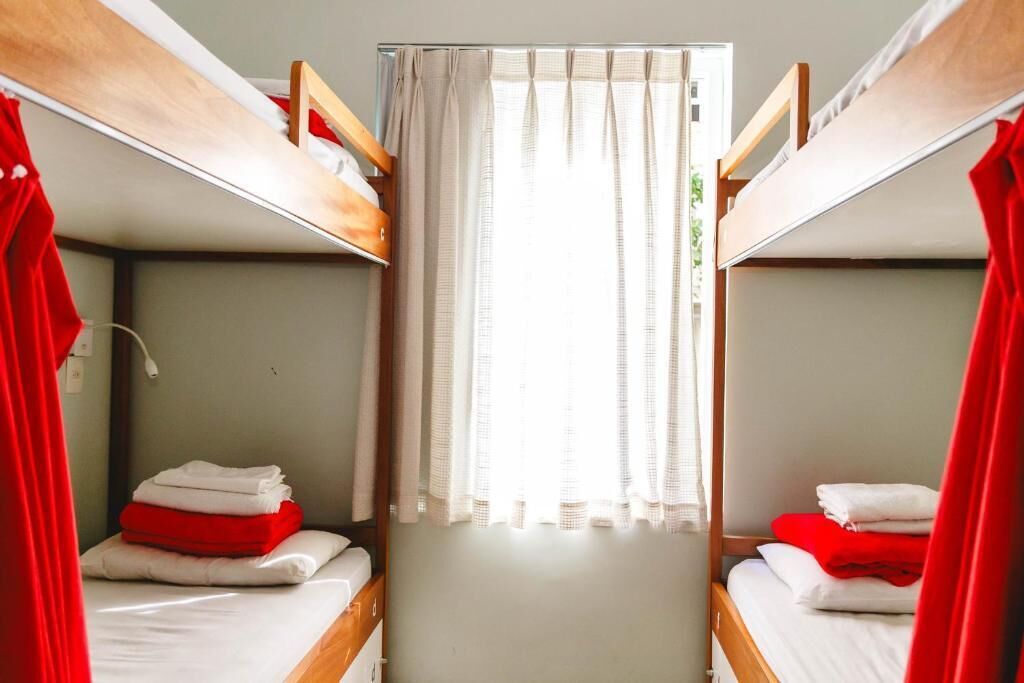 Habitación con literas, dos camas cada una con una manta roja y blanca, y una ventana con cortinas.