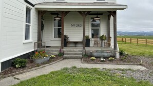 A two-story house with a porch, numbered 2821, featuring a garden with flowers and plants, wooden chairs, and a view of the countryside. - Farmhouse in beautiful Ferndale. Big enough for the whole family! (Ferndale)
