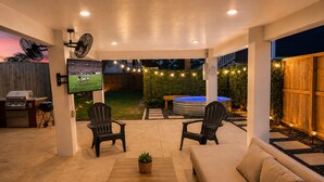Een buitenterras met een televisiescherm, twee Adirondack-stoelen, een bank, een hottub en een barbecue.