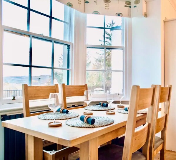 A dining area with a wooden table and chairs, large windows with a view of trees, and a ceiling with circular light fixtures.