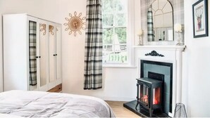A bedroom with a bed, a wardrobe, a fireplace, a window with curtains, and a mirror on the wall. - Gleddoch Coach House offers an exclusive retreat near Glasgow. (Langbank)