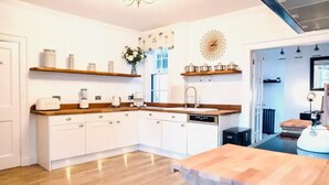 A modern kitchen with white cabinetry, wooden countertops, and built-in appliances. There are decorative shelves above the counter and a large decorative wall piece. - Gleddoch Coach House offers an exclusive retreat near Glasgow. (Langbank)