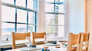 A dining table with wooden chairs and woven placemats, set against a window with a view of trees and hills. - Gleddoch Coach House offers an exclusive retreat near Glasgow. (Langbank)