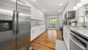 A modern kitchen with stainless steel appliances, white cabinetry, and a wooden floor.