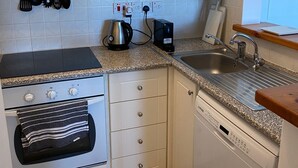 A compact kitchen with white cabinets, a stove, an oven, a dishwasher, a sink, and a countertop. - Regina Gardens 1, Venus Beach -6 min, Sunset Sea View, Gated Complex (Paphos)