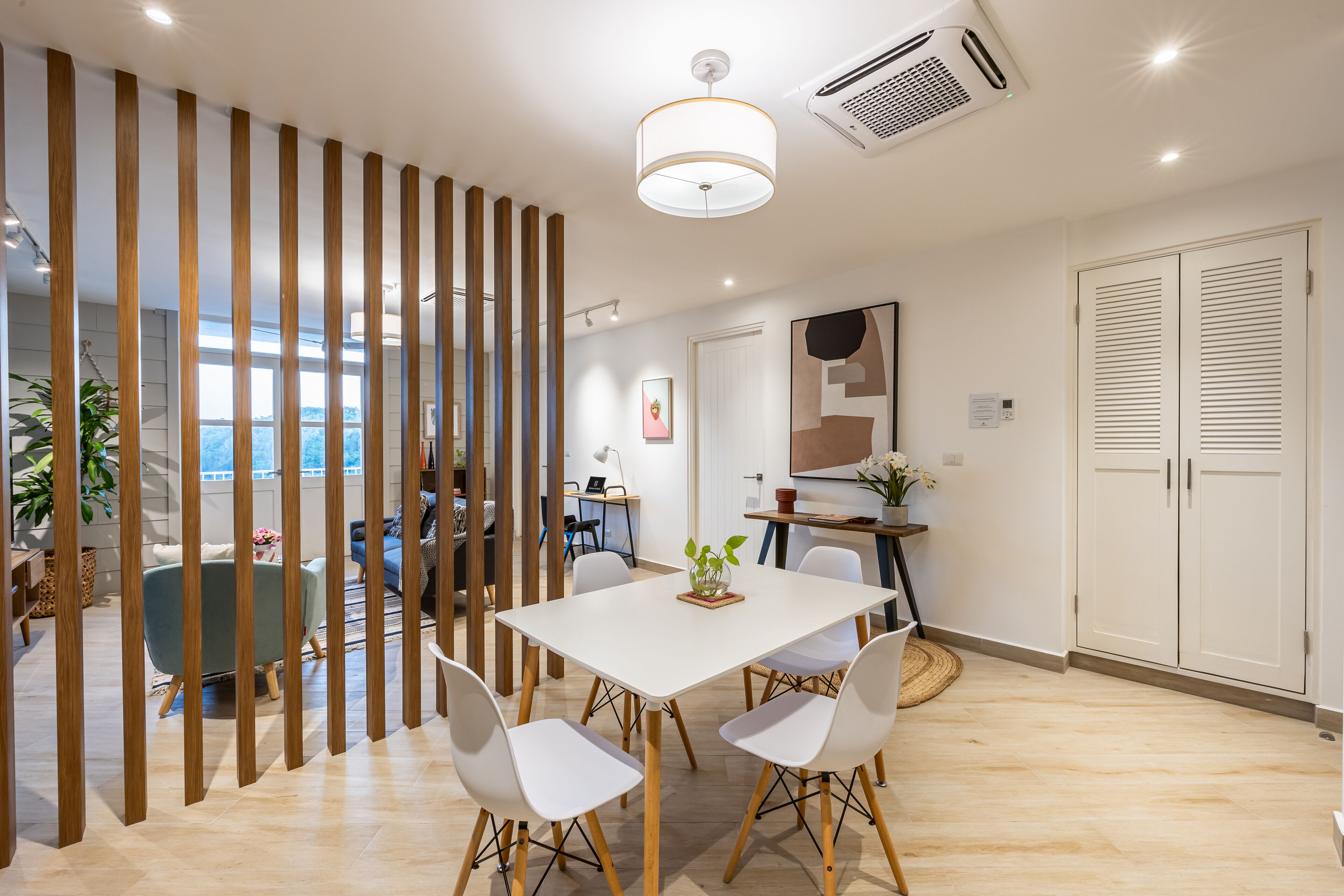 A modern dining area with a white table and chairs, a wooden partition, and a view of the outdoors.