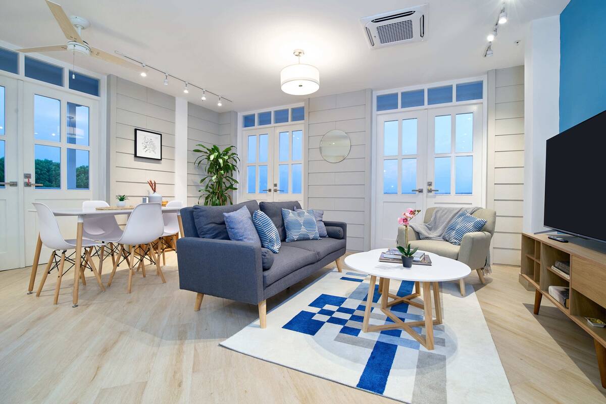 A modern living room with a sofa, coffee table, and TV. There is a dining area with chairs and a table.