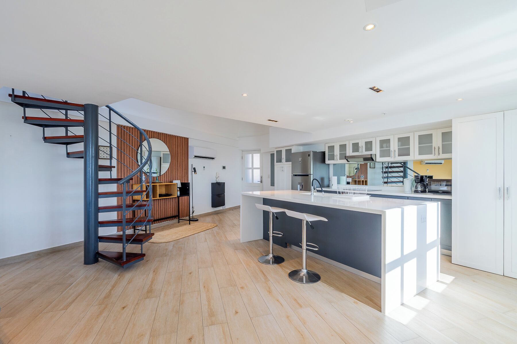Una cocina moderna con una isla central, una escalera en espiral y vistas al salón.