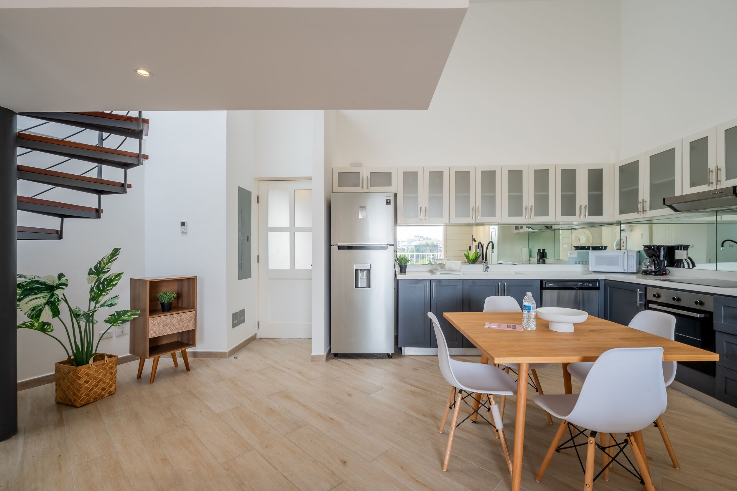 Una cocina moderna con comedor, que presenta una mesa de madera, sillas blancas, un refrigerador y armarios.